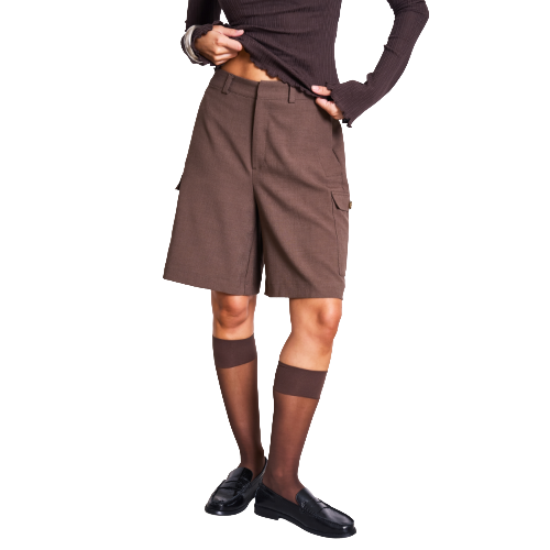 Person wearing a long-sleeve brown top, brown knee-length shorts, sheer brown knee-high socks, and black loafers, standing against a white background. Their face is not visible.