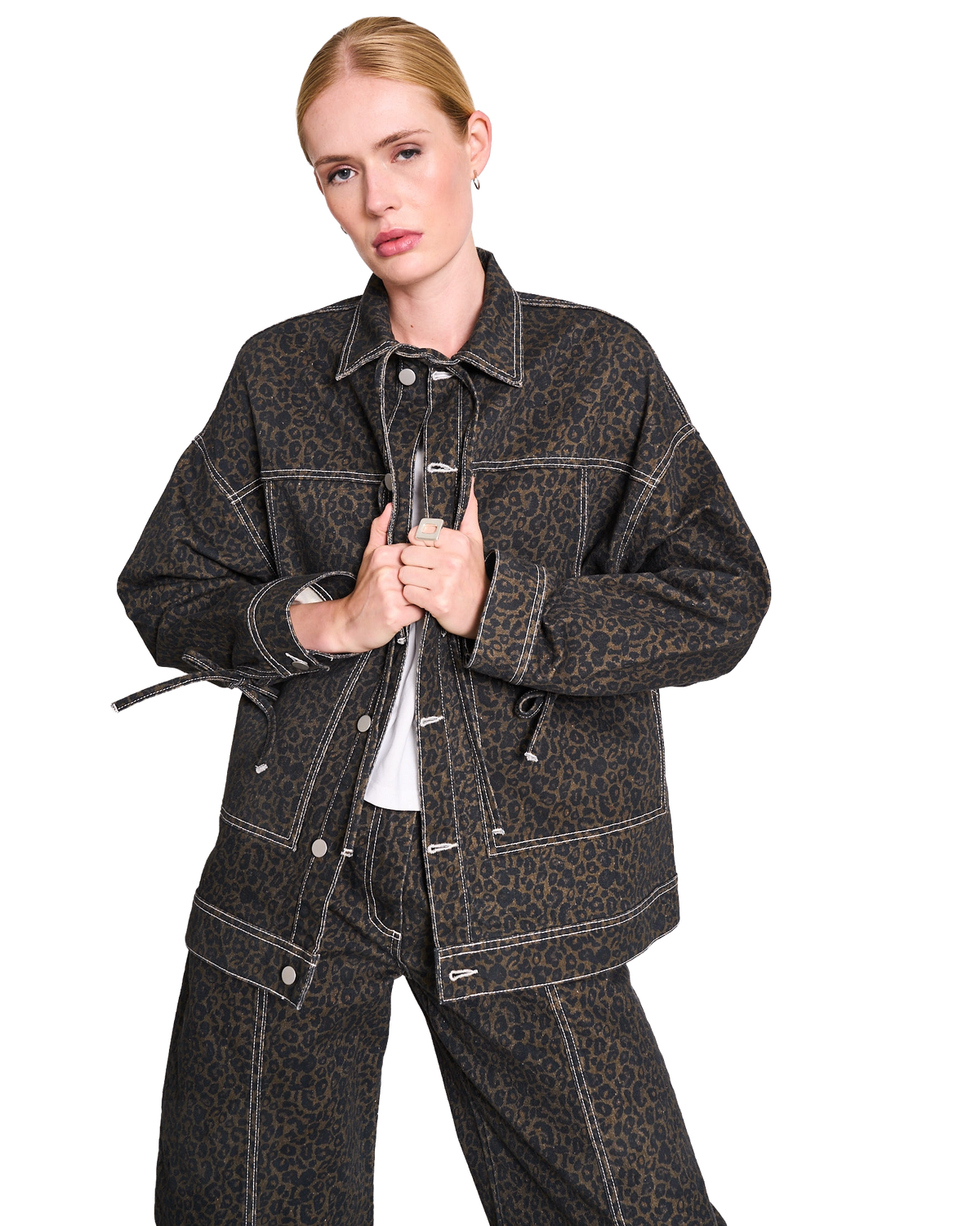 A woman poses in black sunglasses, a black oversized blazer, turtleneck, skinny pants, and pointed heels against a white background.