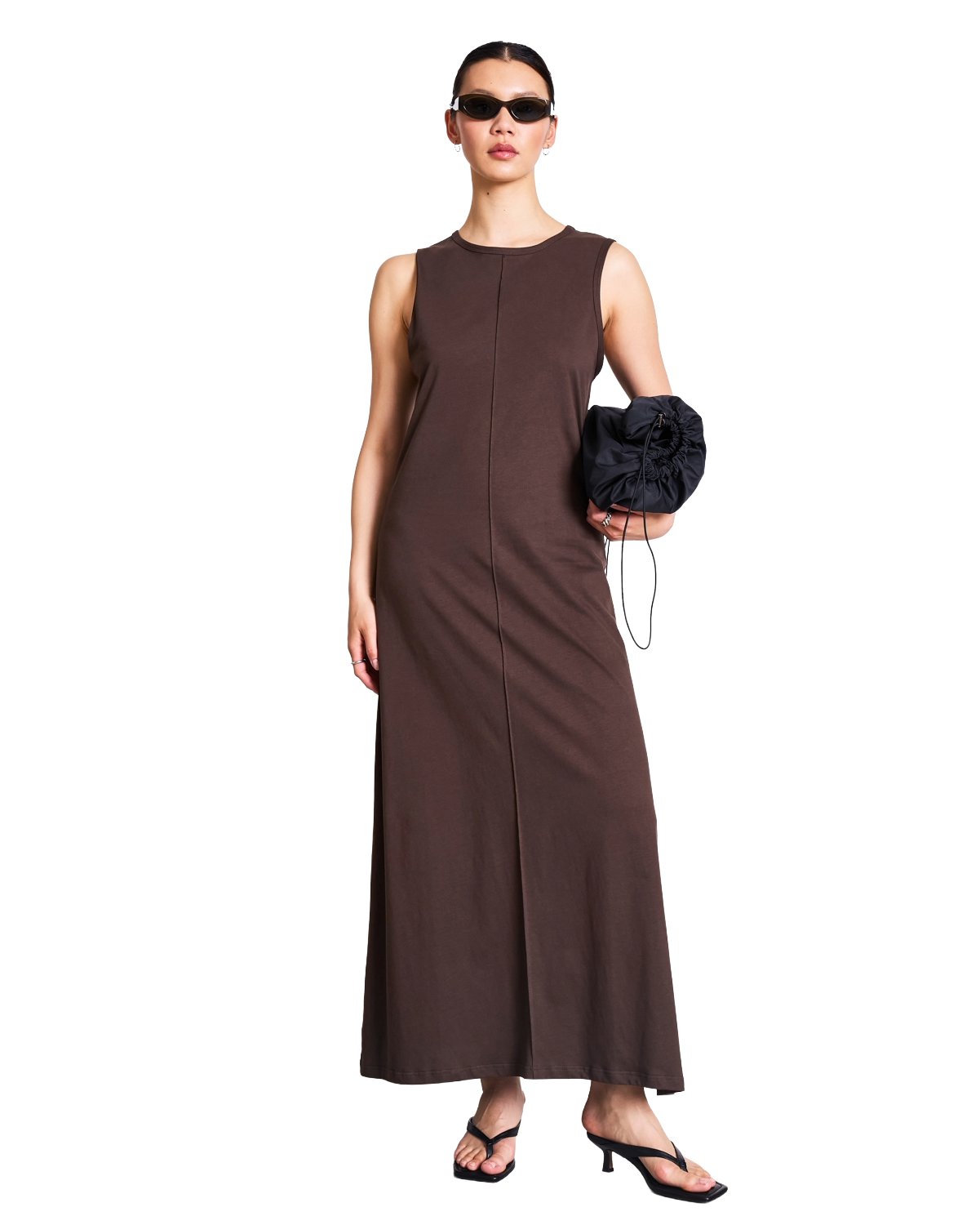 Woman in sunglasses wears a white, V-neck, puff-sleeve maxi dress with a front tie, black boots, and holds a black handbag, standing against a white background.