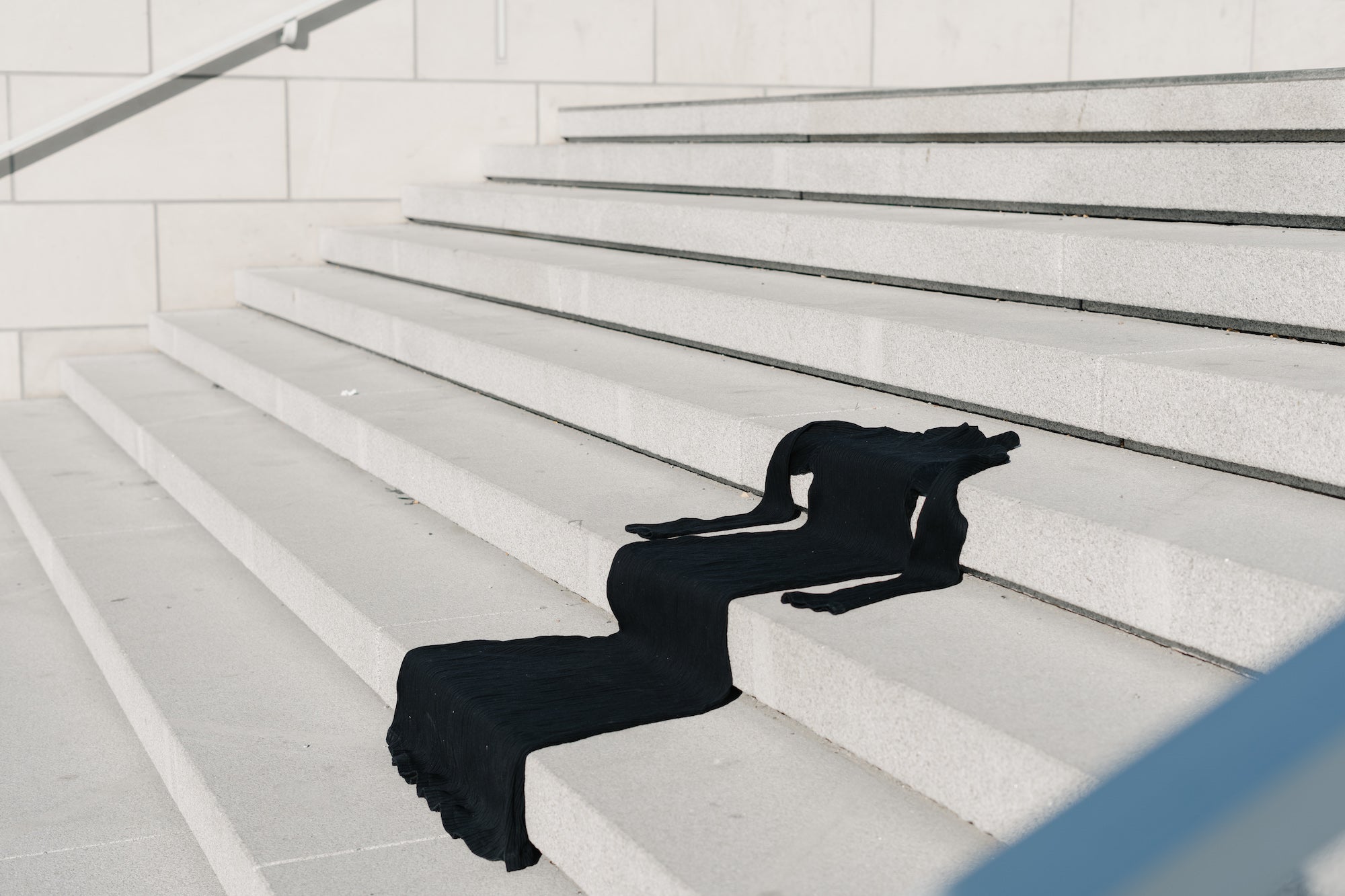 Black turtleneck longsleeve dress draped across light gray concrete stairs.