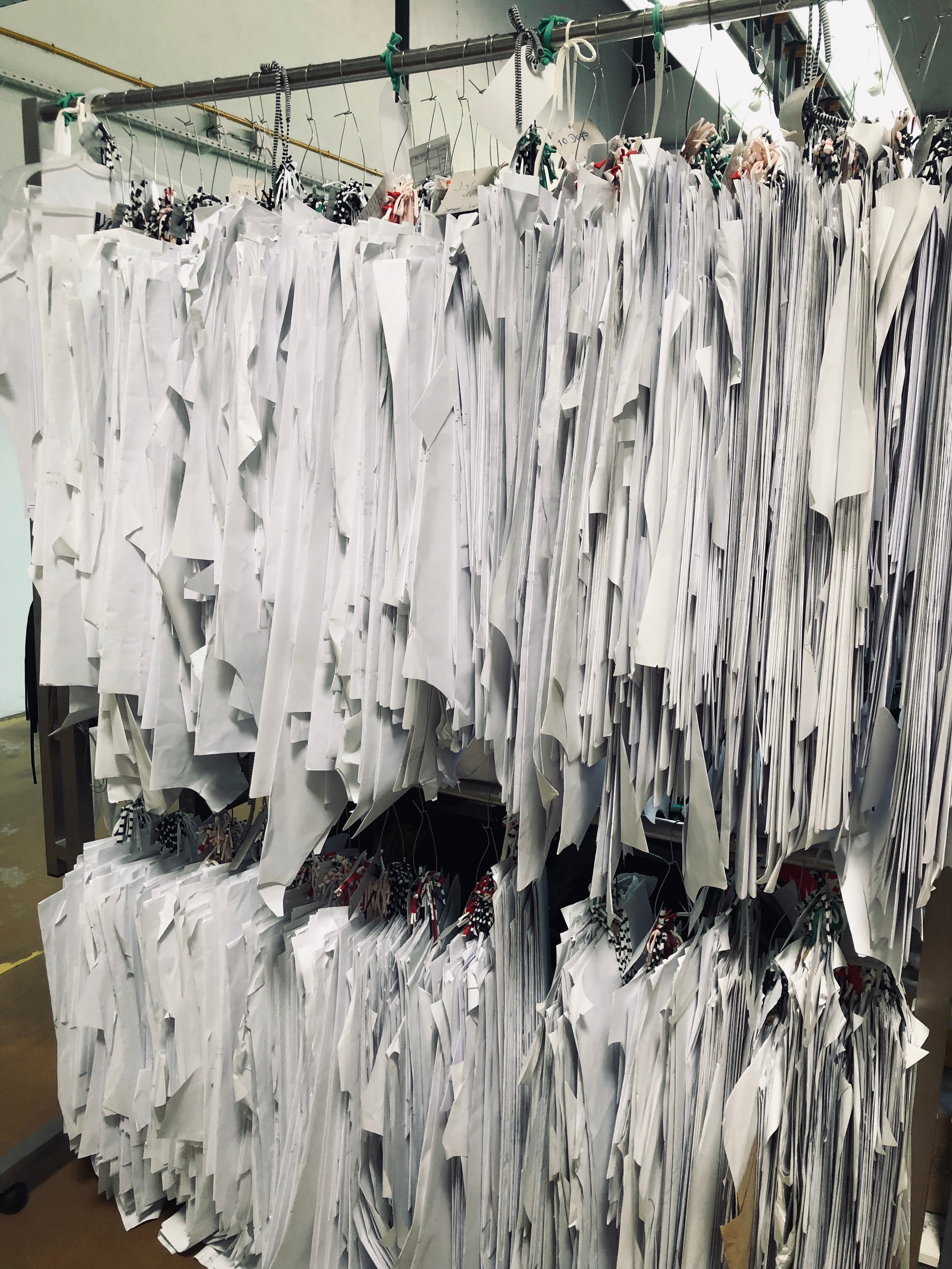 Rows of garment pattern pieces hanging on metal rods, grouped on hangers in a workshop setting.
